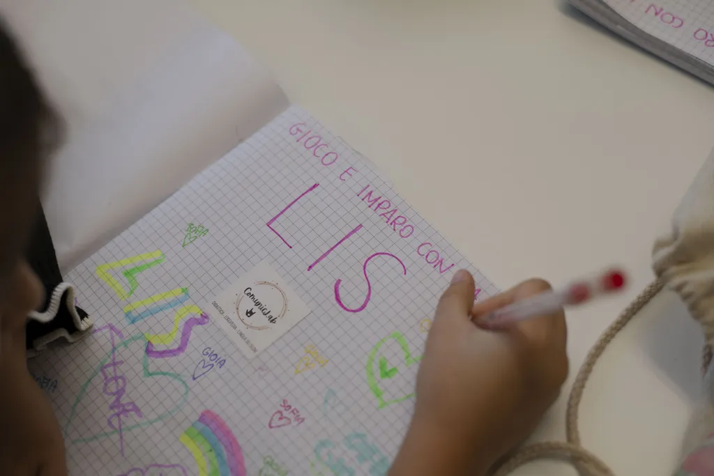 Bambino disegna su quaderno durante attività bambini per servizi educativi e riabilitativi inclusivi.